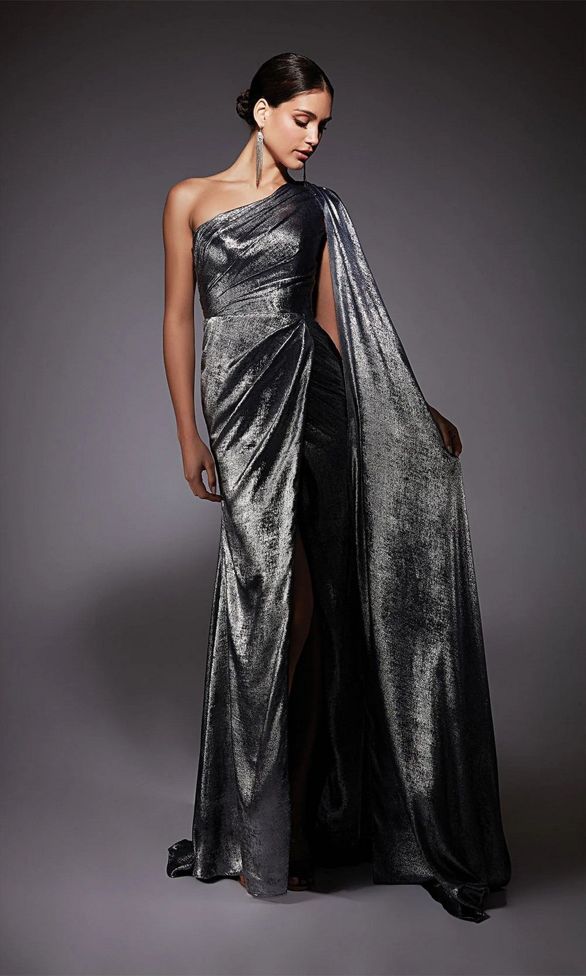 A woman stands against a dark background wearing the Alyce 27753 long formal dress in graphite, featuring a one-shoulder design, draped chiffon fabric, and a floor-length train.